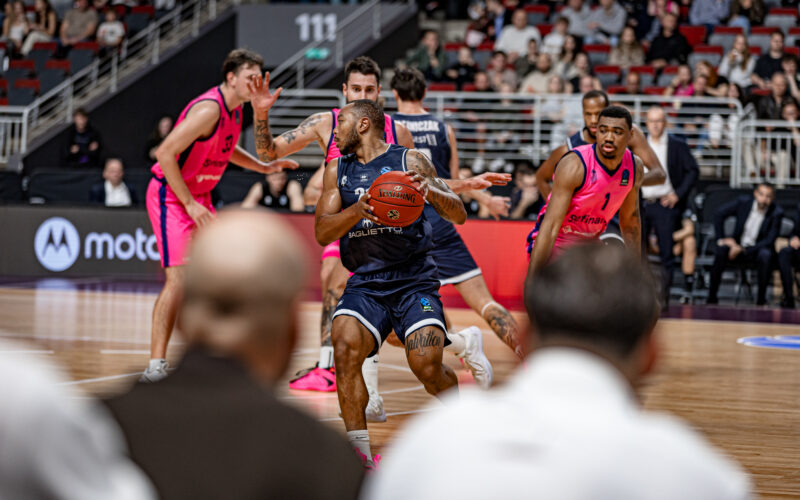 Giocatore di basket Dante Maddox con la palla in mano durante una partita tra Baglietto Derthona Tortona e Le Mans Sarthe, con avversari e pubblico sullo sfondo.