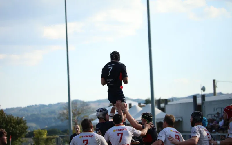Giocatori di rugby in azione durante una partita in campo aperto con paesaggio collinare sullo sfondo.