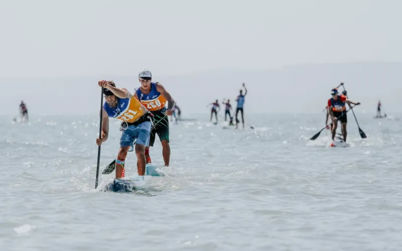 Atleti che gareggiano in Stand Up Paddle su un lago, con vari partecipanti al remo in equilibrio sulle tavole.