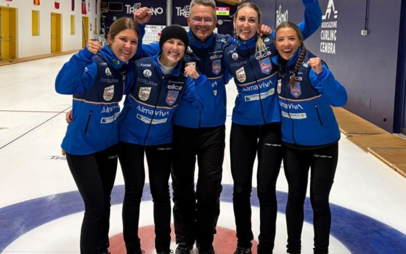 Squadra femminile di curling del Team Dolomiti Zardini Lacedelli Almaviva che festeggia su una pista di curling, indossando divise blu e posando con i pugni alzati.