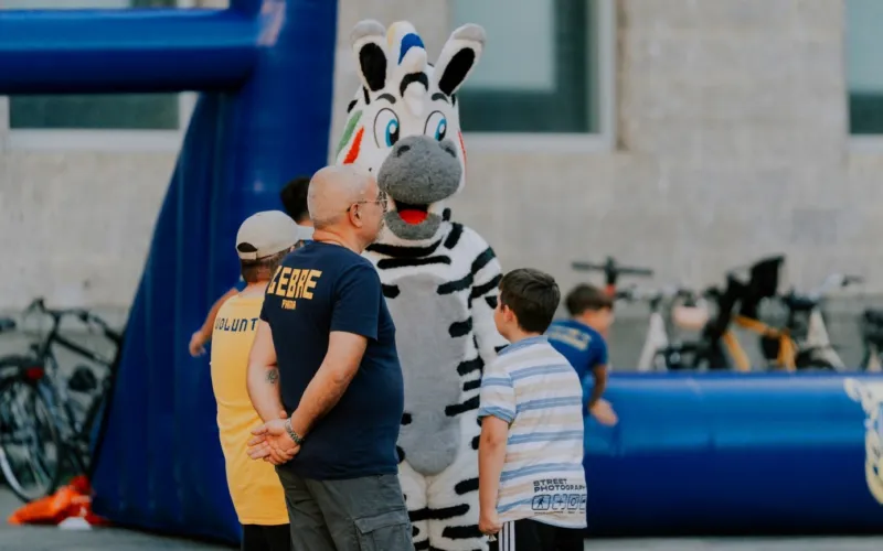 Una mascotte a forma di zebra e alcune persone accanto a una struttura gonfiabile blu.