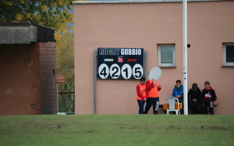 Un tabellone con la scritta «Rugby Gubbio» e il punteggio 42-15; alcune persone sono vicino alla linea laterale.