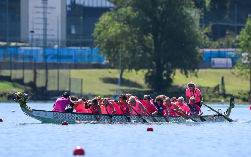 Una squadra di donne in maglia rosa pagaia su una dragon boat in acqua.